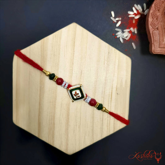 A single rakhi with red threads , red and black beads and a central square charm with a leaf design