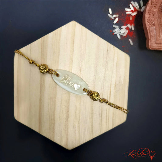 Resin rakhi with "Bhai" written on it , clear oval centerpiece , golden chain thread , on a light wooden background
