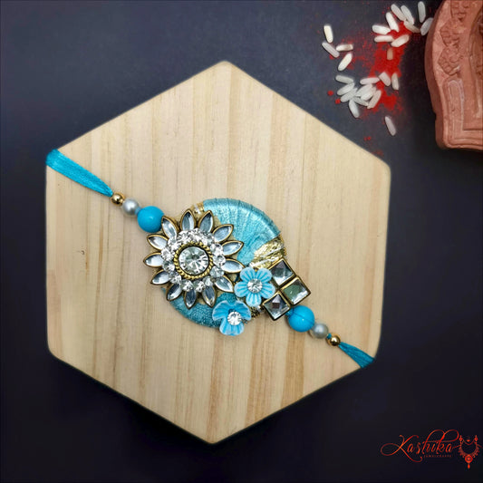 Sky Blue rakhi with a round thread base , adored with clear Kundan floral design and blue beads , on a light wooden surface