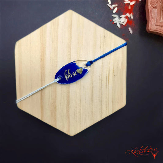 Blue Resin Rakhi with "Bhai" written in gold script and a small heart , clear oval charm , blue and white thread , on a light wooden surface
