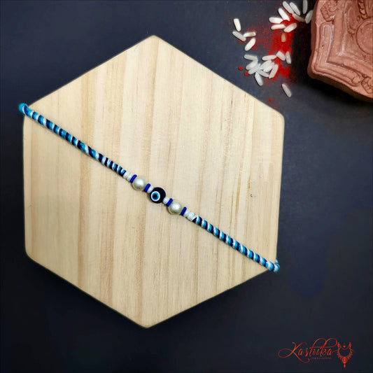 Blue and white single eil eye rakhi on a light wooden hexagon , with rice grains and kumkum in the background