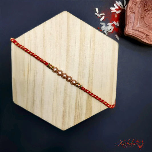 Red rakhi with five light-colored pearls and small golden accents at the center , on a wooden hexagon
