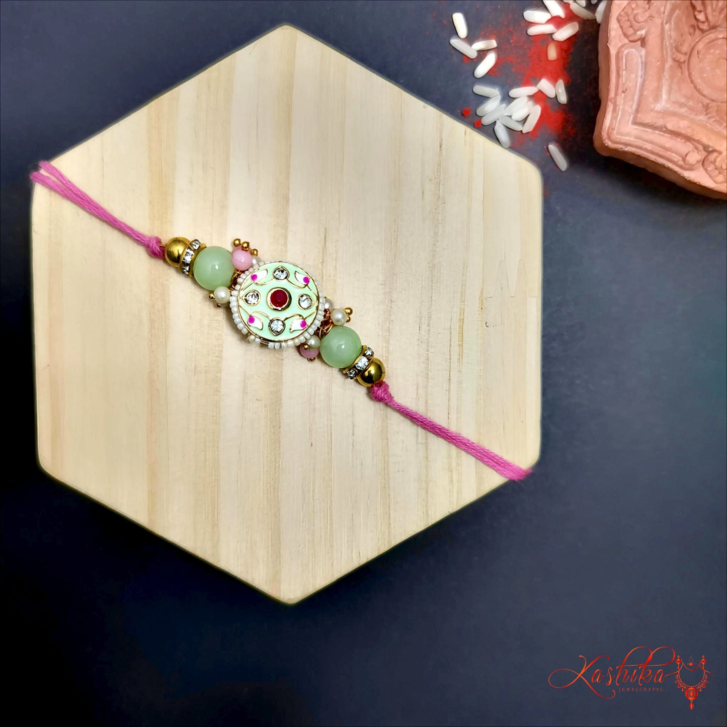 Pista green rakhi with circular white meenakari centerpiece and green beads , on a light wooden hexagon