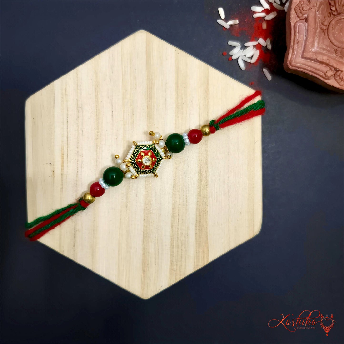 Traditional rakhi with green and red thread , a golden hexagonal centerpiece and green and red beads , on a wooden board