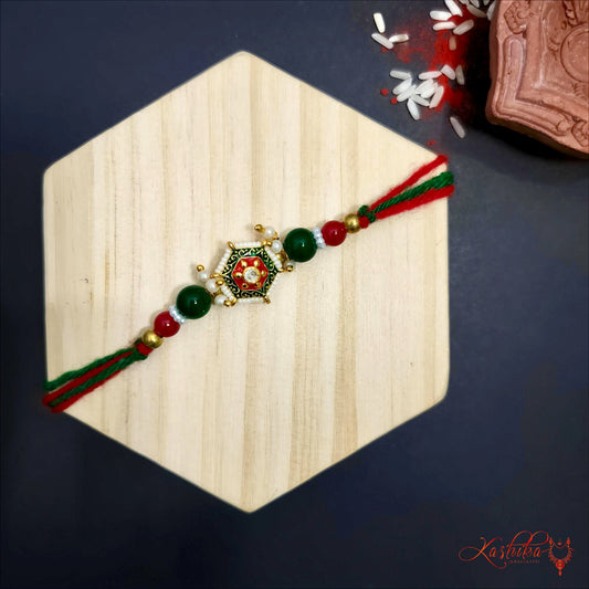 Traditional rakhi with green and red thread , a golden hexagonal centerpiece and green and red beads , on a wooden board