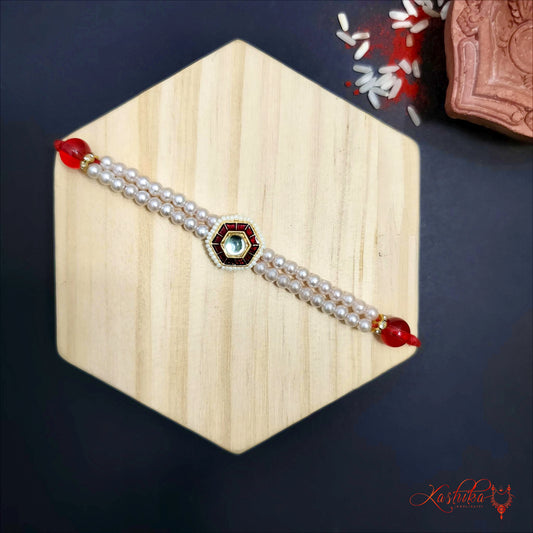 Rakhi with double lines of white pearls , a central kundan stone and red beads on a light wooden hexagon