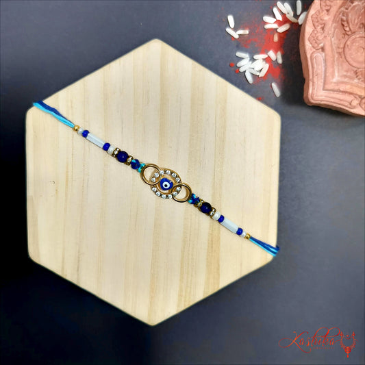 Blue Evil Eye Rakhi with golden rings and blue and white beads on a light brown hexagonal surface for Raksha Bandhan