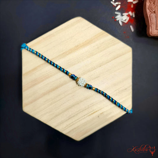 Blue and gold beaded rakhi with a floral centerpiece , displayed on a beige hexagonal surface