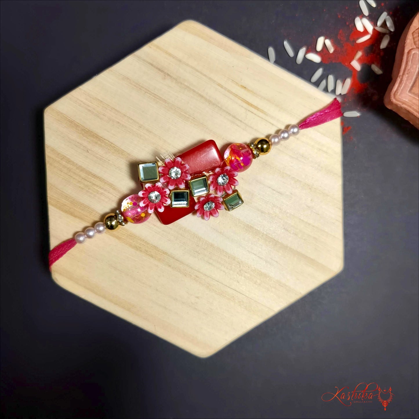 Red stone - studded rakhi with floral and geometric designs , displayed on a light brown surface