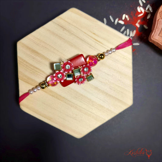 Red stone - studded rakhi with floral and geometric designs , displayed on a light brown surface