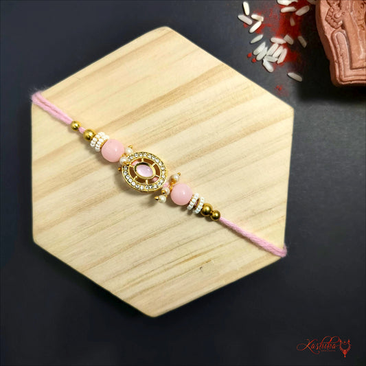 Light pink kundan rakhi with a central pink stone surrounded by golden beads on a light wooden surface