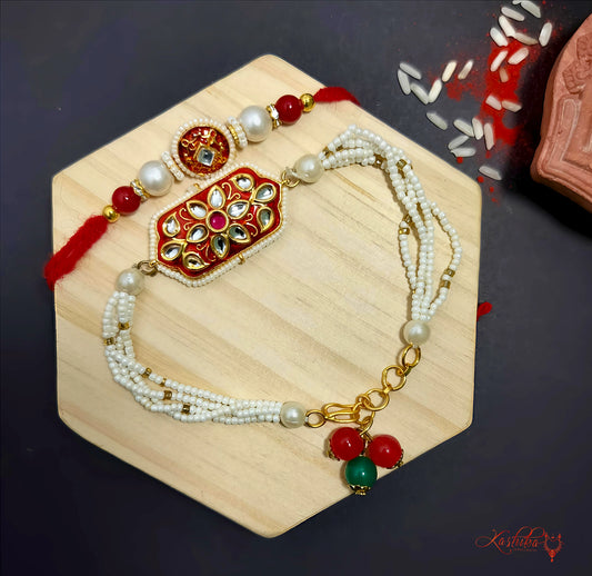 Red and white kundan couple Rakhi set with re-wearable pearl bracelet for female and a traditional rakhi for brother , displayed o a wooden base with rice grains and kumkum