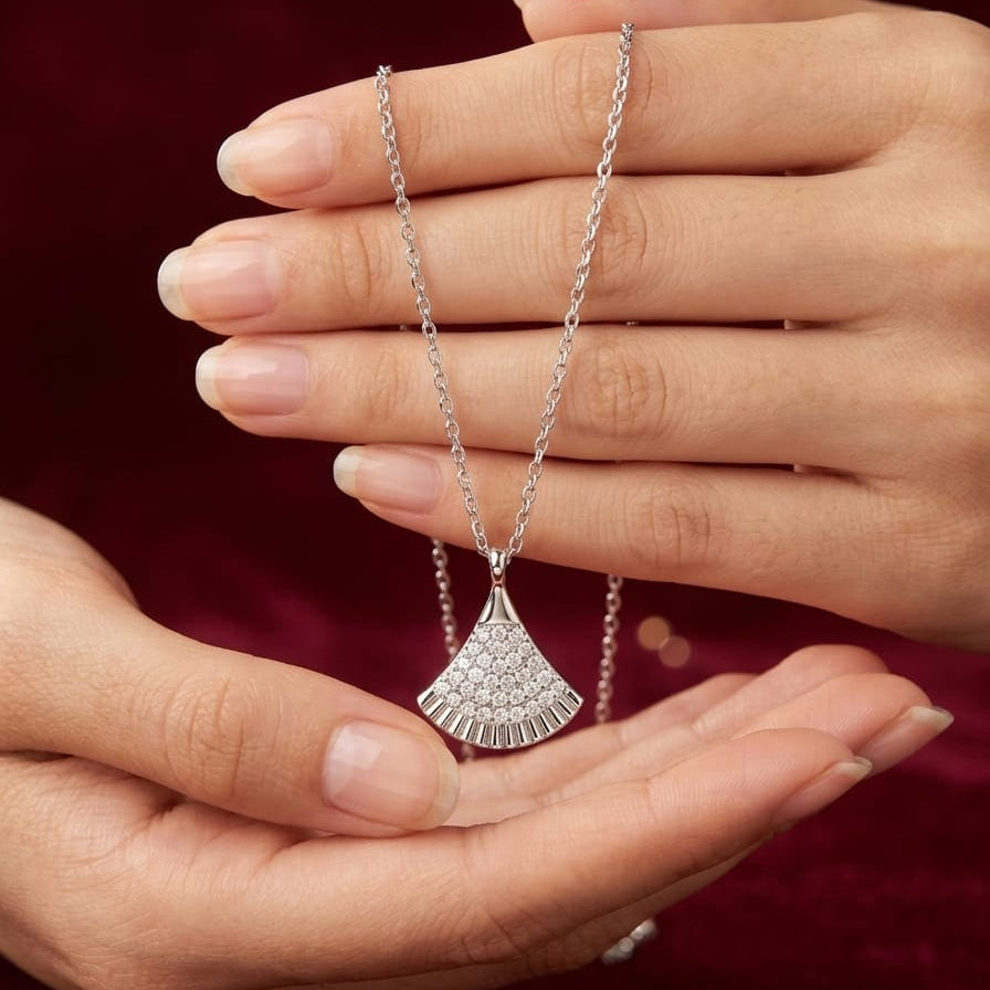 Silver necklace with a fan-shaped pendant held between two hands against a red background