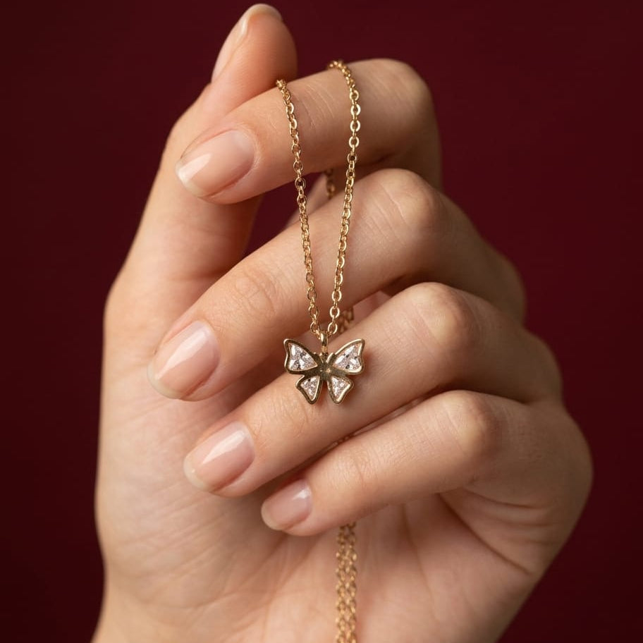 Hand holding a gold necklace with a butterfly pendant against a red background