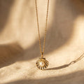 Gold necklace with a shell pendant on a beige fabric background