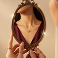 Person holding a vintage mirror reflecting a burgundy dress and gold necklace.