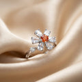 Silver ring with a central orange gemstone and pear-shaped diamonds on beige fabric