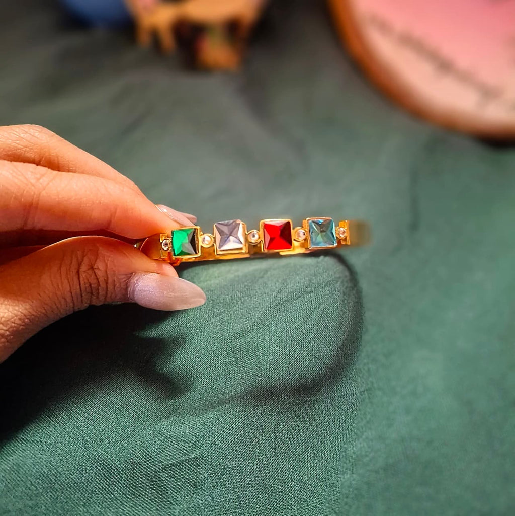 Hand holding a gold bar with colorful gemstones on a green fabric background