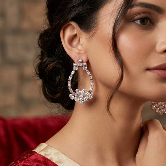 Woman wearing large, ornate earrings with a neutral background