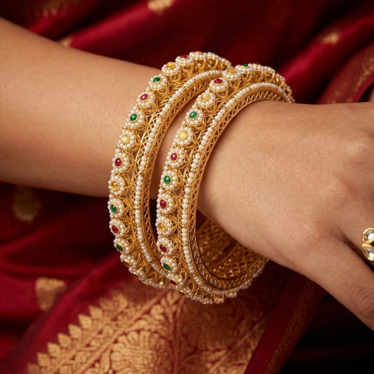 Gold bangles with gemstones on a hand against a red saree background