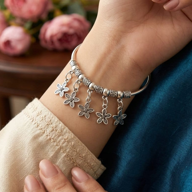 Close-up of a hand wearing a silver bracelet with floral charms, with flowers in the background.