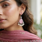Woman wearing traditional attire with a pink scarf and earrings, with a blurred decorative background.