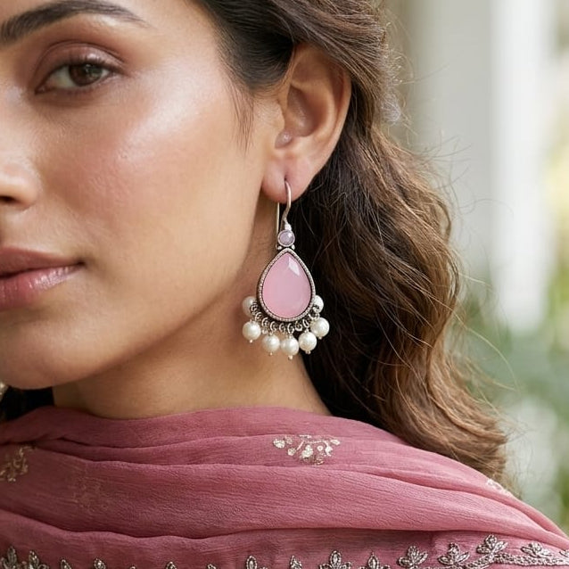 Woman wearing traditional attire with a pink scarf and earrings, with a blurred decorative background.