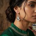 Woman wearing a green traditional outfit with intricate patterns, focusing on her earrings.