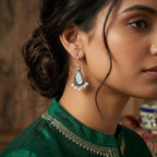 Woman wearing a green traditional outfit with intricate patterns, focusing on her earrings.