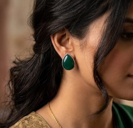 Woman wearing green earrings and a gold necklace with a blurred background