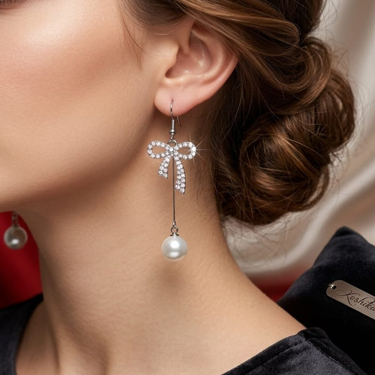 Close-up of a woman wearing pearl earrings with a bow design, against a neutral background.