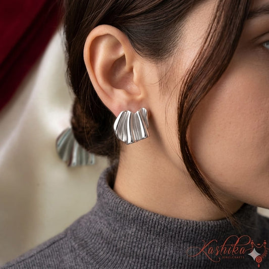 Close-up of a person wearing silver leaf-shaped earrings with a blurred background.