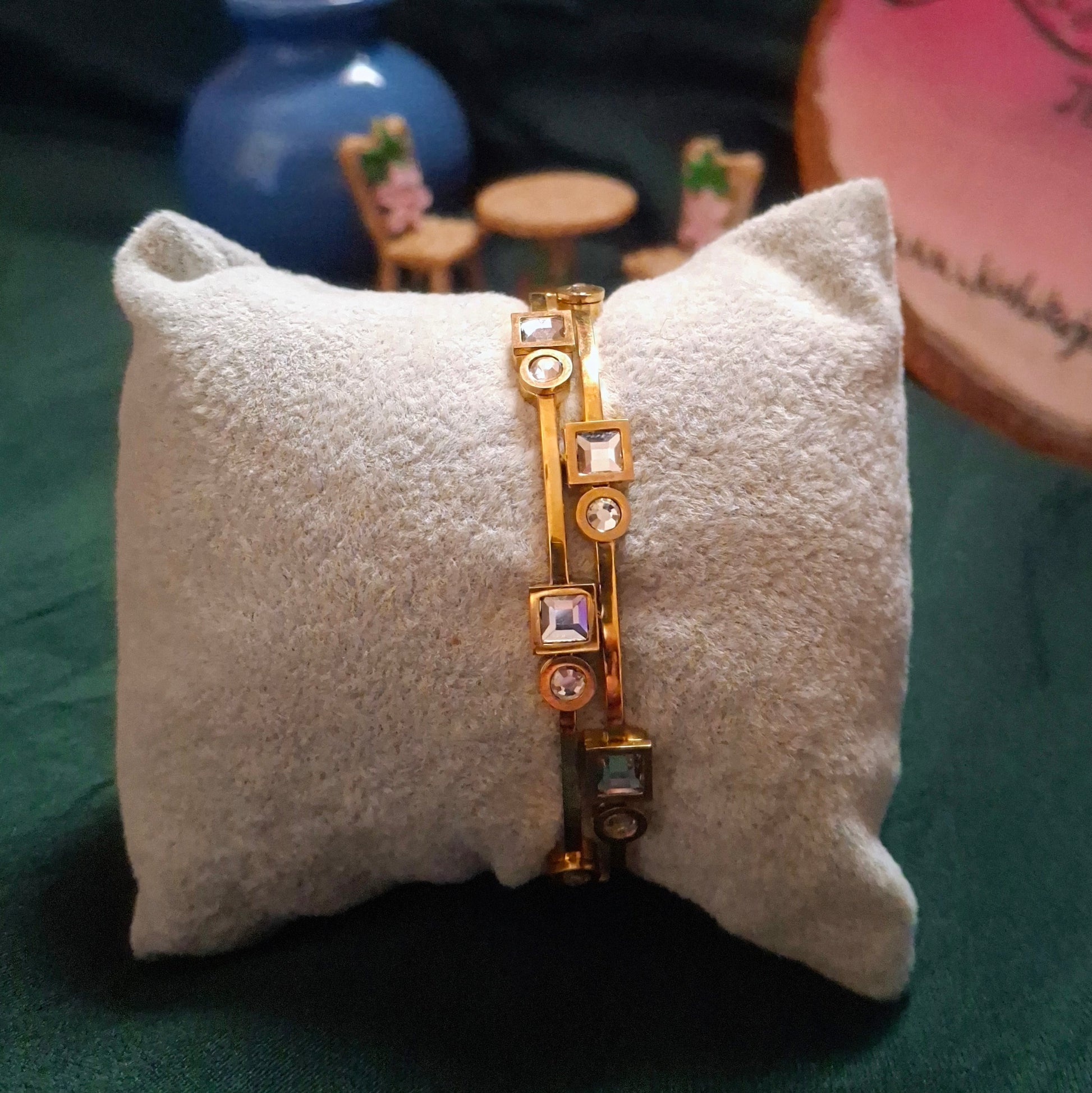 Gold bracelet with gemstones on a white cushion against a dark background