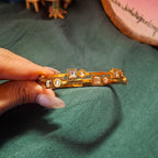 Gold bracelet with gemstones held by a hand on a green fabric background
